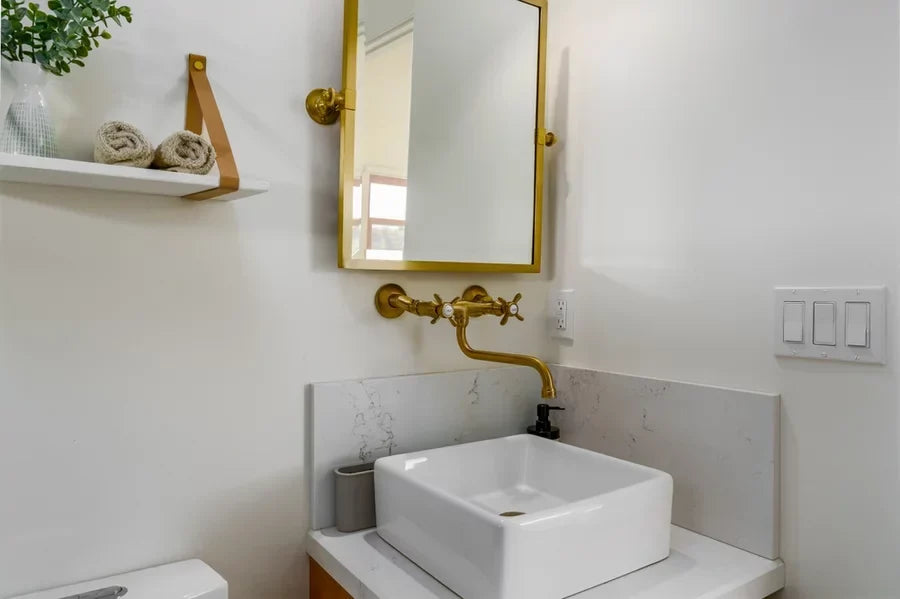Modern bathroom with white ceramic sink, gold brass antique faucet, and mirror